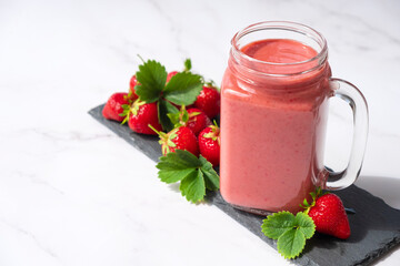 Strawberry smoothie or milkshake on slate dish with fresh strawberry fruit and green leaves on marble background. Recipe of strawberry drink in jar mug full of vitamins and antioxidants.