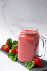 Strawberry smoothie or milkshake on slate dish with fresh strawberry fruit and green leaves on marble background. Recipe of strawberry drink in jar mug full of vitamins and antioxidants.