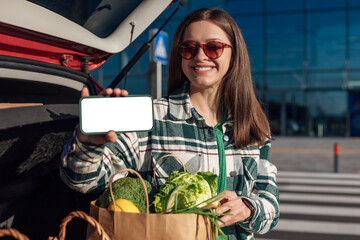 Woman sitting in car's trunk with the shopping paper bags full of groceries