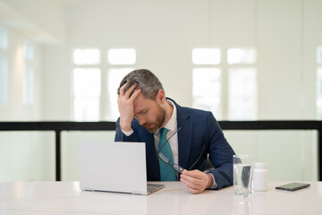 Naklejka premium Headache, tiredness and stress. Business man in suit uses a laptop, is tired got headache migraine. Headache pain concept. Painful men are stressed at work in office. Stressful and headache.