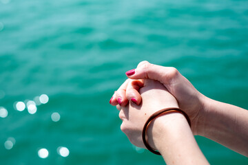 Clasped hands of a girl with nail polish on her fingers and the sea in the background