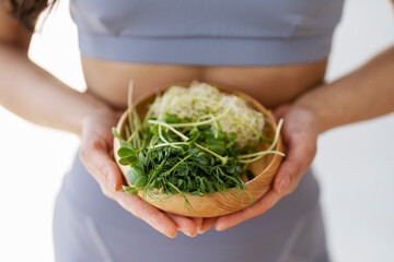 Fit woman holding bowl with fresh micro green standing in modern kitchen