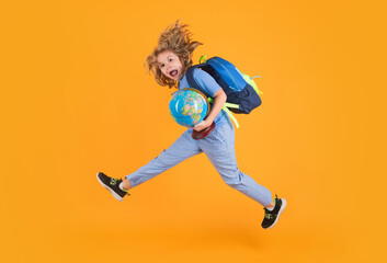 Shool kid jump with school bag and globe. School child in school uniform with bagpack and globe jump. School children jumping on studio isolated yellow background.