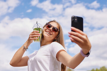 young girl drinks a refreshing cocktail, close-up against the sky