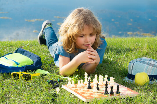 Concentrated child boy developing chess strategy, playing board game in backyard, laying on grass.