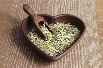 Dry organic background or texture of rosemary leaves. Healthy food concept . a wooden spoon with rosemary, a kind of green color and very fine sticks. leaning on a brown table.