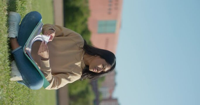 Young teenage Latina college student studying for an exam in an outdoor park with books, vertical shot