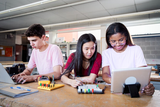 Group Of Three Young Students From A Technical High School Doing A Technological Team Project. People Using The Computer Consulting Doubts About Their Practices In Electronic Technology Class.