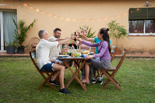 Group of middle-aged friends toast with wine gathered around a garden table on a summer evening to share a meal and have a good time together. High quality photo