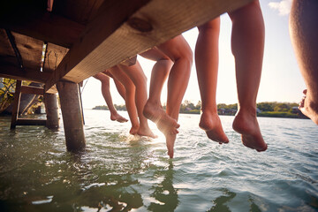 friends sitting on the dock and  enjoying together at vacation dangling legs in the water - 604176464