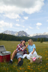A happy couple is having a picnic on a meadow at the mountains. Relationship, nature, activity, love