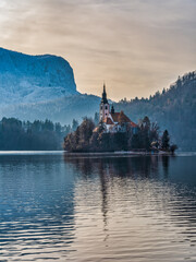 Vertical shot of shot of Assumption of Maria Church island in the middle of lake bled and snow the...