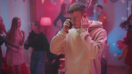 A guy at a party in a decorated room with a disco ball is talking on the phone while his friends...