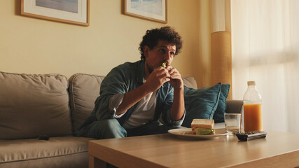 Guy dressed in denim shirt has lunch, sits in the living room and emotionally watches sports game...