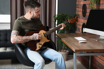 Obraz premium Handsome hipster man playing guitar in stylish room