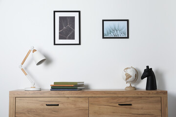 Desk lamp, books and decor on wooden chest of drawers indoors