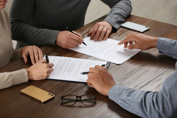 Notary helping couple with paperwork at wooden table, closeup