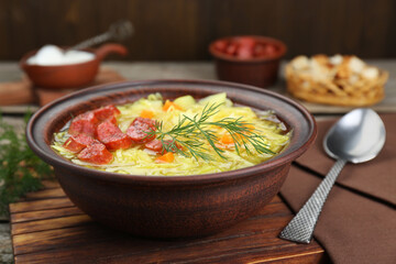 Bowl of delicious sauerkraut soup with smoked sausages and dill on wooden board