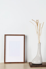 Empty photo frame and vase with dry decorative spikes on wooden table. Mockup for design