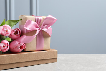 Beautiful gift box with bow and pink tulip flowers on light table, space for text