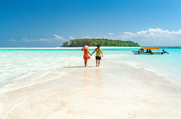 Man and woman in love holding hands walking on empty sandy shore surrounded by the Indian Ocean, Zanzibar, Tanzania