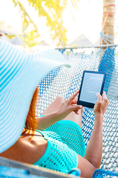 Cheerful woman on a hammock enjoying reading a digital book on tablet, Zanzibar, Tanzania