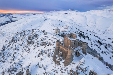 Aerial winter view of Rocca Calascio castle and the Santa Maria della Pietà church in the snowy landscape at dusk, Campo Imperatore, L'Aquila province, Abruzzo region, Italy
