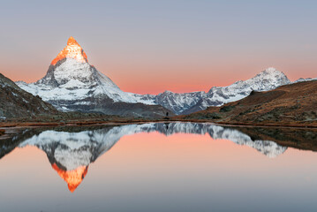 Hiker admiring the Matterhorn reflected in the Riffelsee lake at sunrise, Gornergrat, Zermatt, canton of Valais, Switzerland