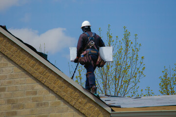 man holding bundle of asphalt shingles working on fixing a roof security rope