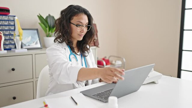 Young beautiful hispanic woman doctor opening laptop working at clinic