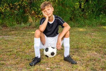 Tired young soccer player sitting on a soccer ball after a game