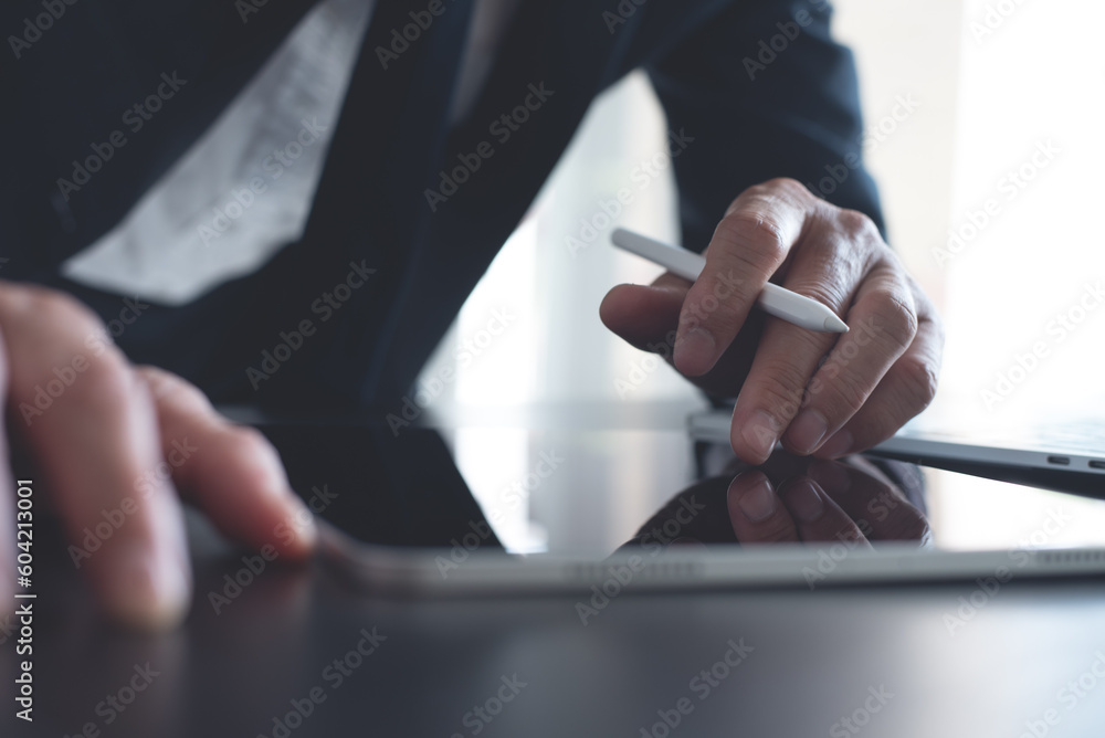 Poster businessman using digital tablet surfing the internet and working on laptop computer on office desk.