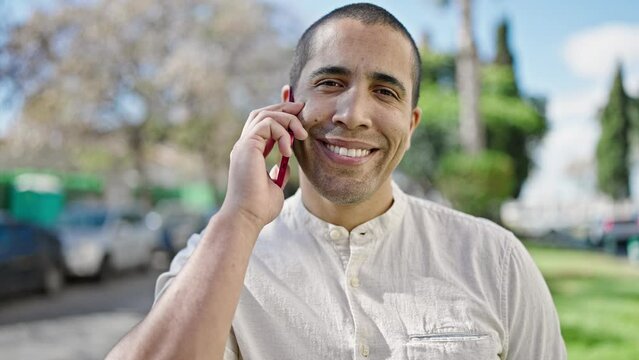Young hispanic man speaking on the phone at park