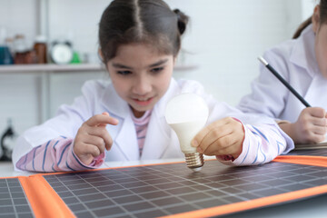 Female students learn about clean energy in class, attention to bulbs and solar panels, eco friendly energy concept