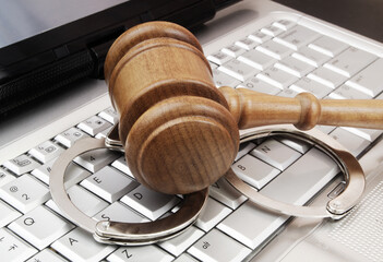 Wooden gavel with handcuffs on laptop keyboard close-up. Concept of laws and cyber security.
