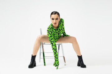 Stylish bright dancer in a bright green leopard print bodysuit, posing on a chair, studio photo on...