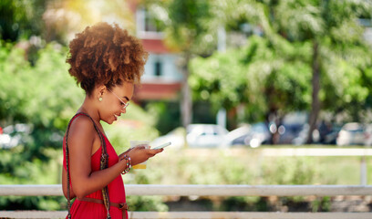 side view young afro girl holding looking at cell phone in a park