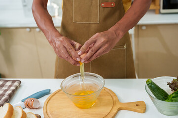 Close-up hands young man cooking in kitchen, was hammering fresh chicken egg rim cup, crack fresh chicken egg into cup, with one chicken egg, wanted cook with simple menu with ingredients at home.