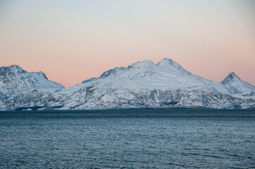 Landscape shot highlighting the rugged mountains and snow-covered beaches of arctic norway during a brief golden hour during the long winters.