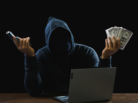 Hacker spy man wearing a black shirt, sitting on a chair and a table, is a thief, hands holding money, counting the amount obtained from hijacking or robbing, in pitch-black room.