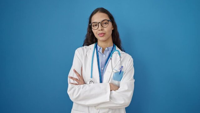 Young beautiful hispanic woman doctor smiling confident standing with crossed arms over isolated blue background