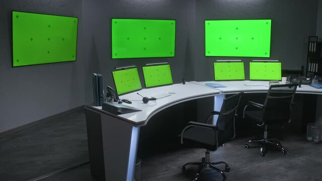 Workspace in security control center for monitoring CCTV cameras. Computer monitors on the table and big digital screens on the wall with chroma key showing surveillance cameras footage. Green screen.