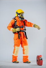 Vertical picture shows a firefighter standing and holding a fire hose while pointing his finger and looking sideways on a white background.