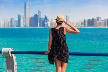 Tourist woman in Abu Dhabi, UAE. Sea, beach and skyscrapers background - obrazy, fototapety, plakaty