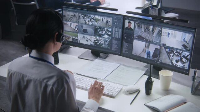 Security officer in headset controls CCTV cameras with AI facial recognition on PC. Female employee works in security control center. Computer monitors showing surveillance cameras video footage.