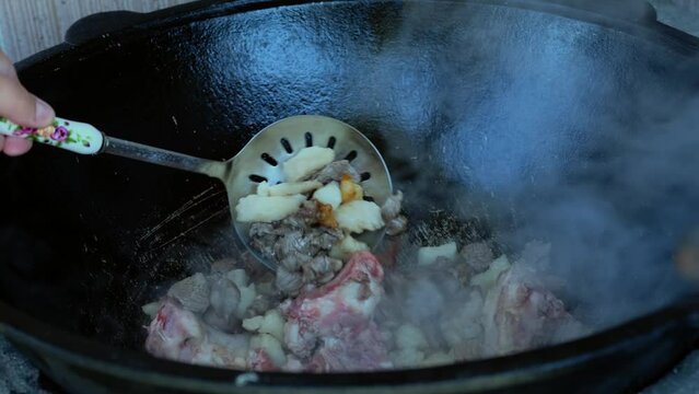 Cooking pilaf in a cauldron, lamb meat with tail fat. Mouth-watering video where a traditional pilaf dish is cooked. Female hand stirs pilaf. Chef uses the lamb meat that's cooked with tail fat. 