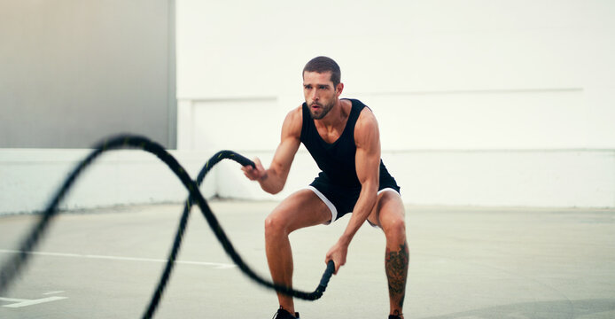 Man, fitness and battle rope exercise for physical training, workout or wellness in the outdoors. Fit, active and serious male person exercising with ropes for intense endurance, stamina or cardio