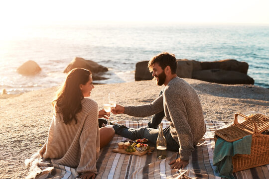 Picnic, beach and couple with champagne happy for relax, bonding and quality time on romantic date. Nature, dating and man and woman toast for anniversary, honeymoon and love on holiday or vacation