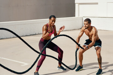Woman, personal trainer and battle rope for workout, exercise or training in fitness outdoors. Fit,...