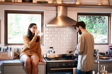 Cooking, couple and wine in a kitchen at home with food at a stove drinking alcohol. Young woman, man and drinks in a house together making dinner with bonding, love and care for eating a meal